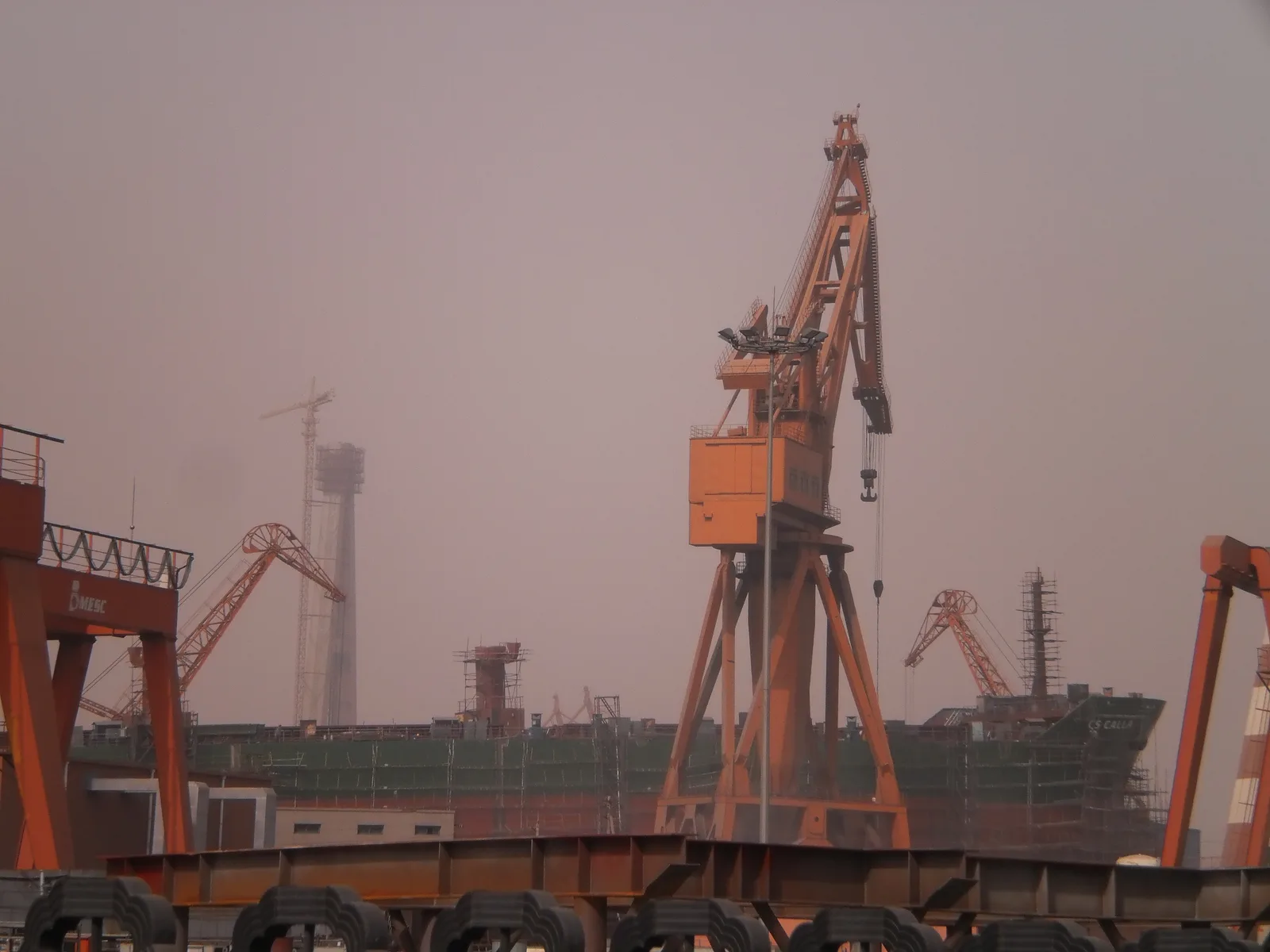 Commercial ship under construction with industrial cranes and fabrication equipment at a shipyard in Tianjin.